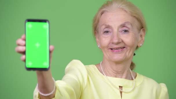 Счастливая пожилая бизнесвумен улыбается, показывая телефон — стоковое видео