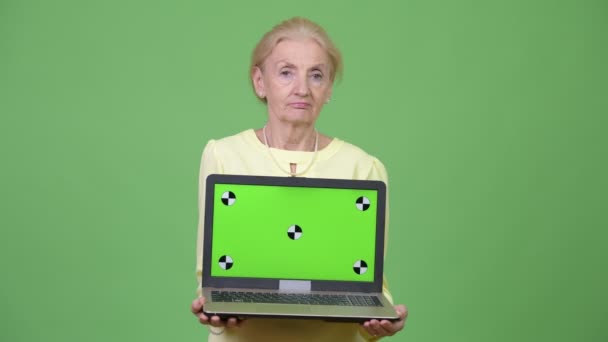 Schöne glückliche Seniorin lächelt, während sie Laptop zeigt — Stockvideo