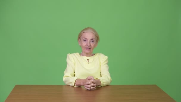 Красива старша бізнес-леді представляє щось проти дерев'яного столу — стокове відео