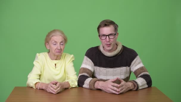 Schläfrige Seniorin und junger gutaussehender Mann präsentieren gemeinsam etwas — Stockvideo