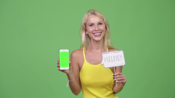 junge glückliche schöne blonde Frau zeigt Telefon mit Papierschild