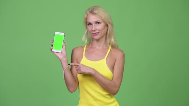 Jovem mulher loira bonita feliz mostrando telefone e dando polegares para cima — Vídeo de Stock
