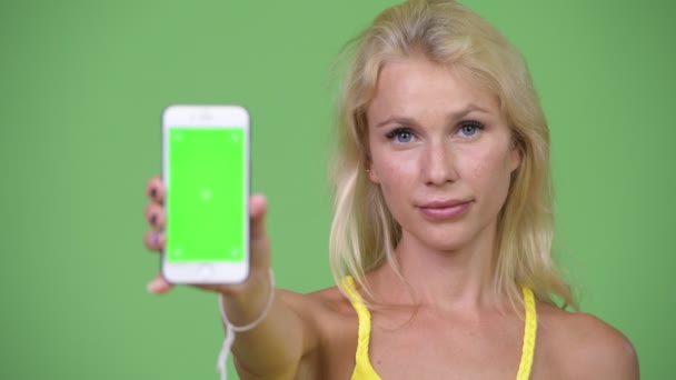 Jovem mulher loira bonita feliz mostrando telefone — Vídeo de Stock