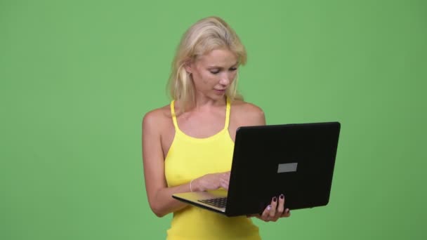 Junge glückliche schöne blonde Frau mit Laptop vor grünem Hintergrund — Stockvideo