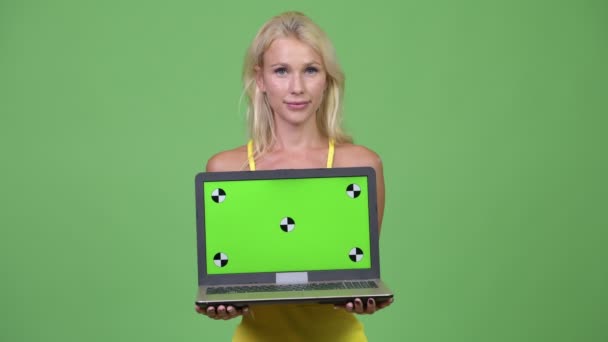 Jovem mulher loira bonita feliz mostrando laptop contra fundo verde — Vídeo de Stock