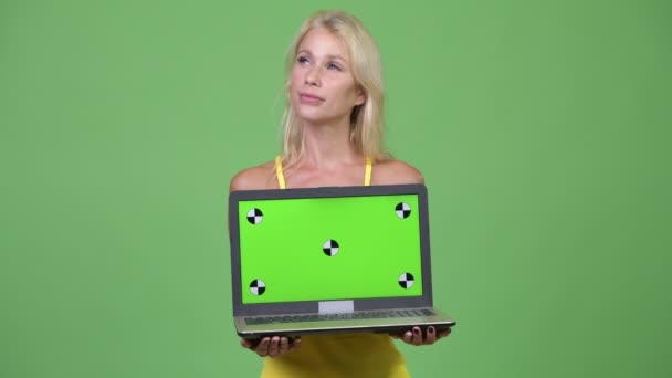 Молода щаслива красива блондинка думає, показуючи ноутбук — стокове відео