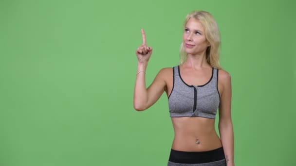 Junge glückliche schöne Frau denkt, während sie nach oben zeigt, bereit für das Fitnessstudio — Stockvideo