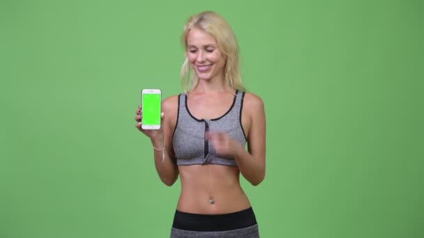 Jovem mulher bonita feliz mostrando telefone e dando polegares para cima pronto para ginásio — Vídeo de Stock