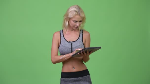 Молодая счастливая красивая женщина думает, используя цифровой планшет готов к тренажерному залу — стоковое видео