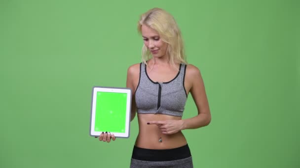 Jovem mulher bonita feliz mostrando tablet digital e dando polegares para cima pronto para ginásio — Vídeo de Stock