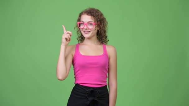 Jovem feliz linda nerd mulher sorrindo enquanto apontando o dedo para cima — Vídeo de Stock