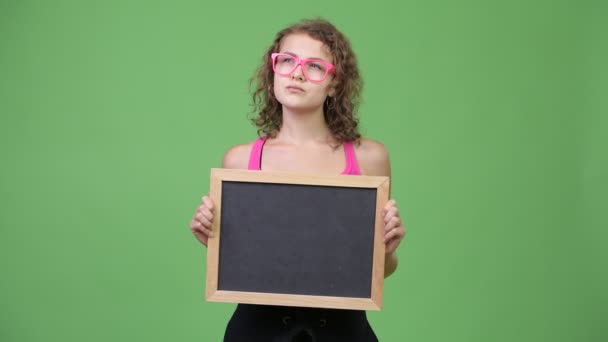 Jovem feliz bela nerd mulher pensando enquanto segurando quadro negro — Vídeo de Stock