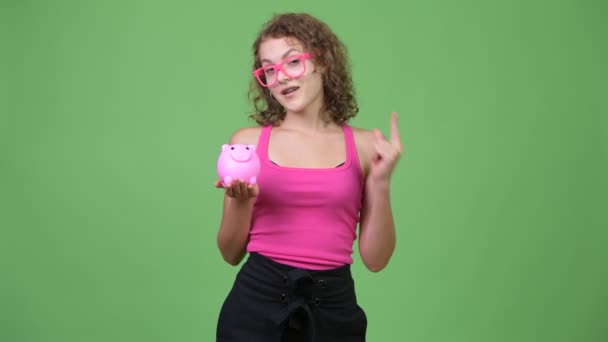 Jovem feliz linda nerd mulher segurando porquinho banco e dando polegares para cima — Vídeo de Stock