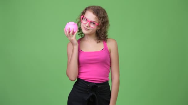 Jonge mooie nerd vrouw denken terwijl het schudden piggy bank — Stockvideo