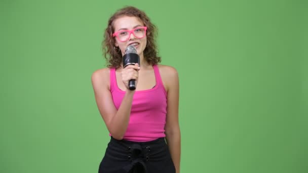 Молодая счастливая красивая ботан женщина представляет что-то с микрофоном — стоковое видео