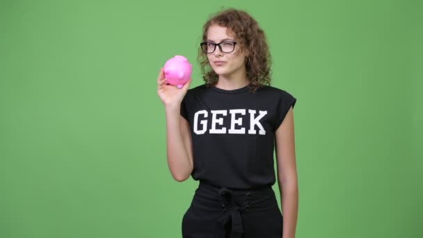 Jonge mooie nerd vrouw denken terwijl het schudden piggy bank — Stockvideo