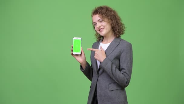 Joven feliz hermosa mujer de negocios mostrando el teléfono y dando pulgares hacia arriba — Vídeos de Stock