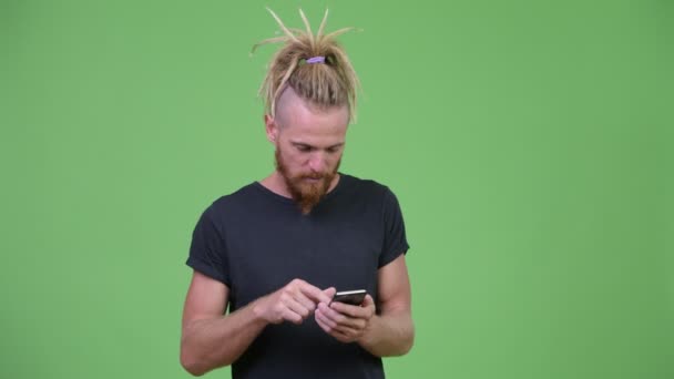 Homem barbudo bonito feliz com dreadlocks usando telefone e recebendo boas notícias — Vídeo de Stock