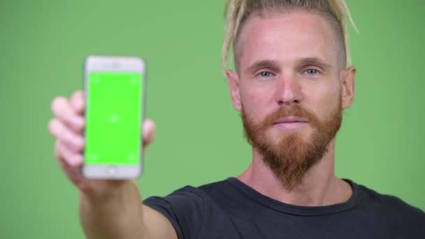Lykkelig, kjekk skjeggete mann med dreadlocks som viser fram telefonen – stockvideo