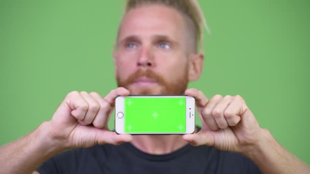 Красивый бородатый мужчина с дредами думает, показывая телефон — стоковое видео