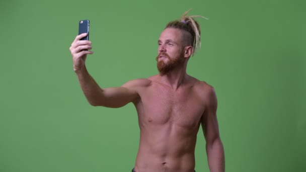 Bonito homem barbudo muscular feliz com dreadlocks tomando selfie enquanto flexionando braço sem camisa — Vídeo de Stock