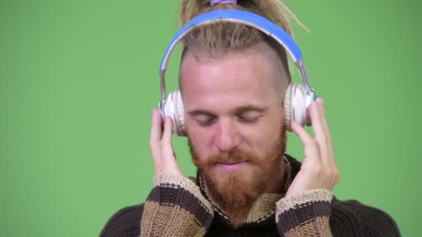 Handsome bearded man with dreadlocks wearing warm clothing while listening to music — Stock Video