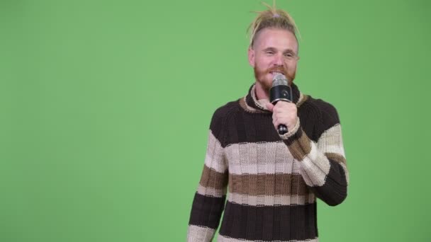 Счастливый красивый бородатый мужчина с дредами представляет что-то с микрофоном — стоковое видео