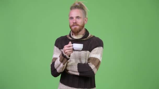 セーターを着ていると、コーヒーを飲みながら考えて幸せなハンサムなひげを生やした男 — ストック動画