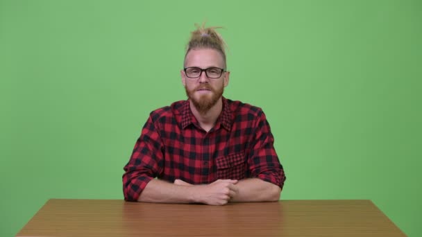 Ευτυχισμένη hipster γενειοφόρος άνδρας χαμογελώντας εναντίον ξύλινο τραπέζι — Αρχείο Βίντεο