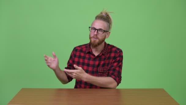 Szép szakállas csípő ember bemutató valami ellen, fából készült asztal — Stock videók