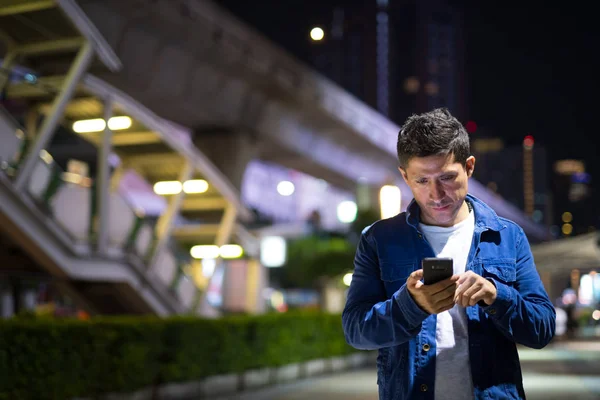 Hispanic man using phone while exploring the city streets at night — Stock Photo, Image