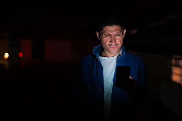 Hombre hispano de aspecto sospechoso usando el teléfono en el estacionamiento oscuro —  Fotos de Stock