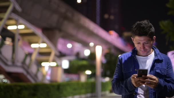 Hispanic man using phone while exploring the city streets at night — Stock Video