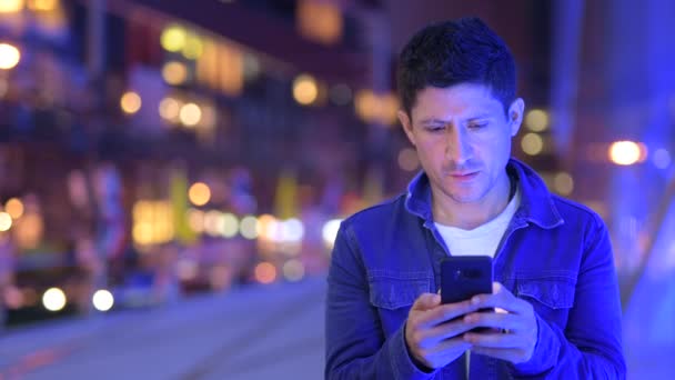 Homem hispânico feliz usando telefone nas ruas da cidade à noite — Vídeo de Stock