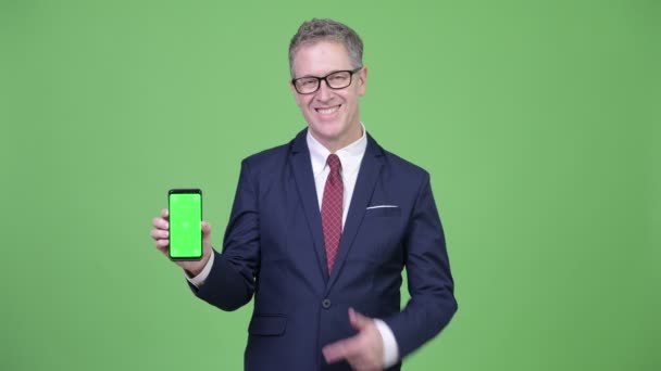 携帯電話を示すと、親指をあきらめて幸せの成熟したビジネスマンのスタジオ撮影 — ストック動画