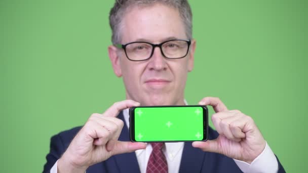 Studio shot of happy mature businessman showing phone — Stock Video