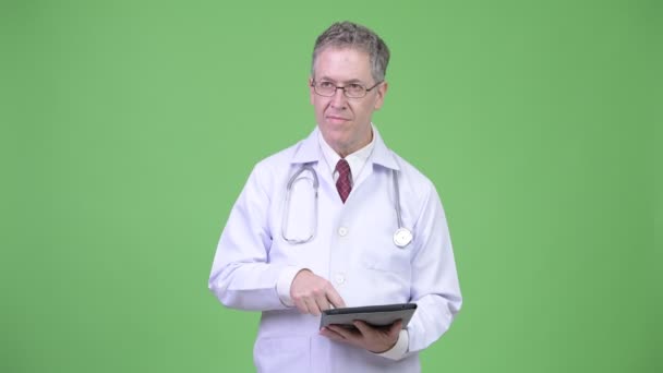 Retrato de hombre maduro feliz médico pensando mientras que la tableta digital — Vídeo de stock