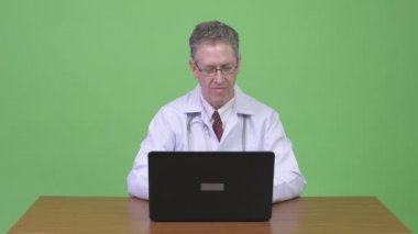 Ahşap masa karşı laptop kullanırken düşünerek mutlu olgun adam doktor portresi