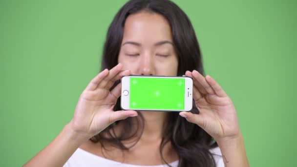 Unga glada vackra multietniska kvinna tänker samtidigt visar telefonen — Stockvideo
