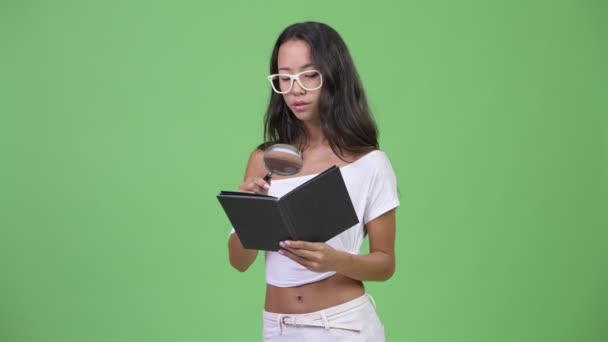 Молодая красивая многонациональная женщина читает книгу с увеличительным стеклом и очками — стоковое видео