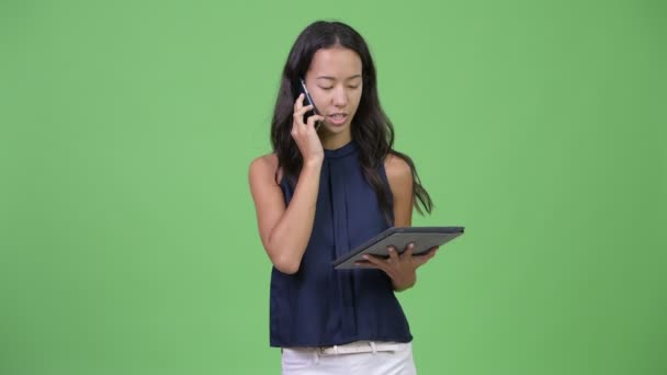 Junge schöne multiethnische Geschäftsfrau, die mit Telefon und digitalem Tablet arbeitet — Stockvideo