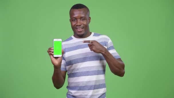 Giovane felice uomo africano mostrando telefono e puntando il dito — Video Stock