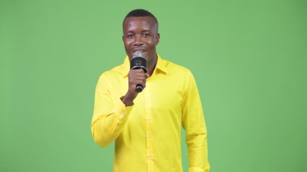Jeune homme d'affaires africain heureux chantant avec microphone — Video