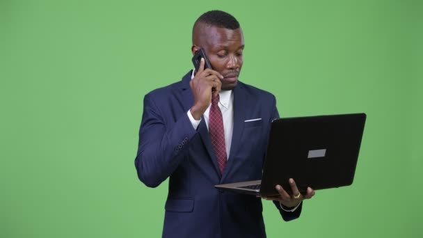 Молодой счастливый африканский бизнесмен разговаривает по телефону с помощью ноутбука — стоковое видео