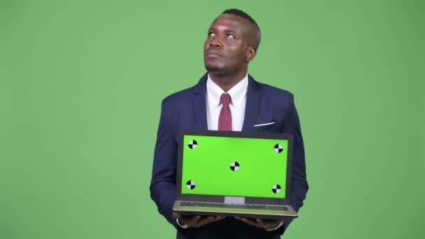 Giovane felice uomo d'affari africano pensando mentre mostra il computer portatile — Video Stock