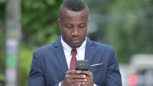 Joven empresario africano feliz usando el teléfono al aire libre — Vídeo de stock