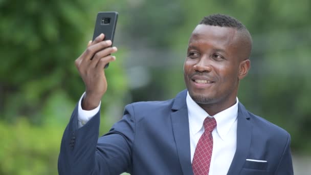 Young happy African businessman taking selfie outdoors — Stock Video