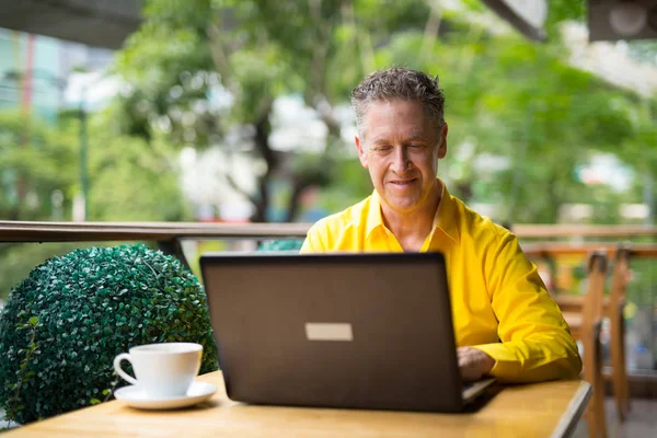 Hombre guapo maduro sentado en la cafetería mientras usa la computadora portátil — Foto de Stock