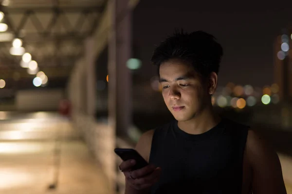 Όμορφος Ασίας νεαρός χρήση του τηλεφώνου κατά την άποψη της πόλης τη νύχτα — Φωτογραφία Αρχείου