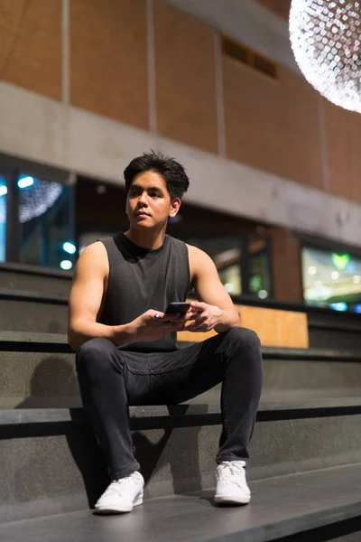 Όμορφος Ασίας νεαρός σκέψης κατά τη χρήση τηλεφώνου στην πόλη ύπαιθρο τη νύχτα — Φωτογραφία Αρχείου